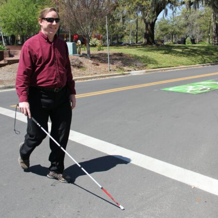 man crossing at cross walk with a cane